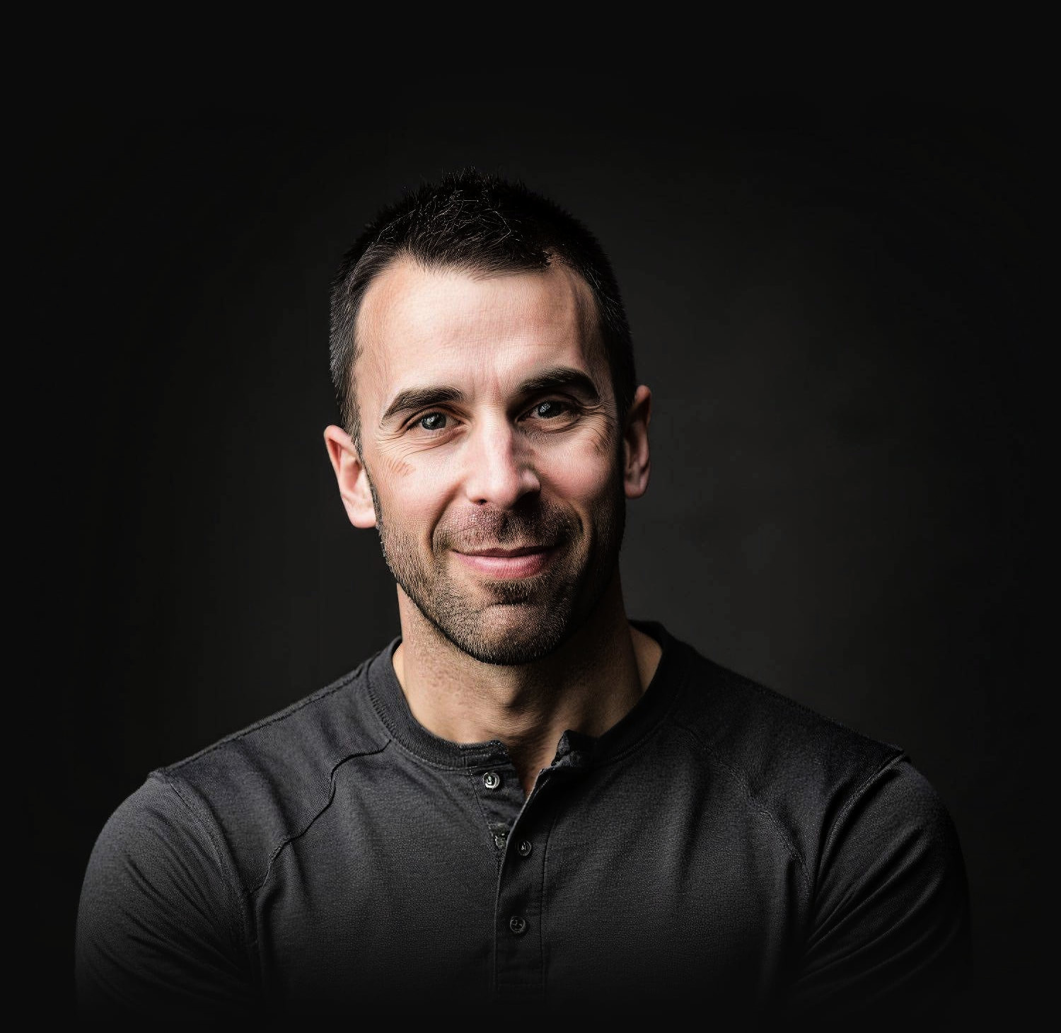 Tony LeBlanc in a charcoal henley against a dark studio backdrop, looking at the camera.