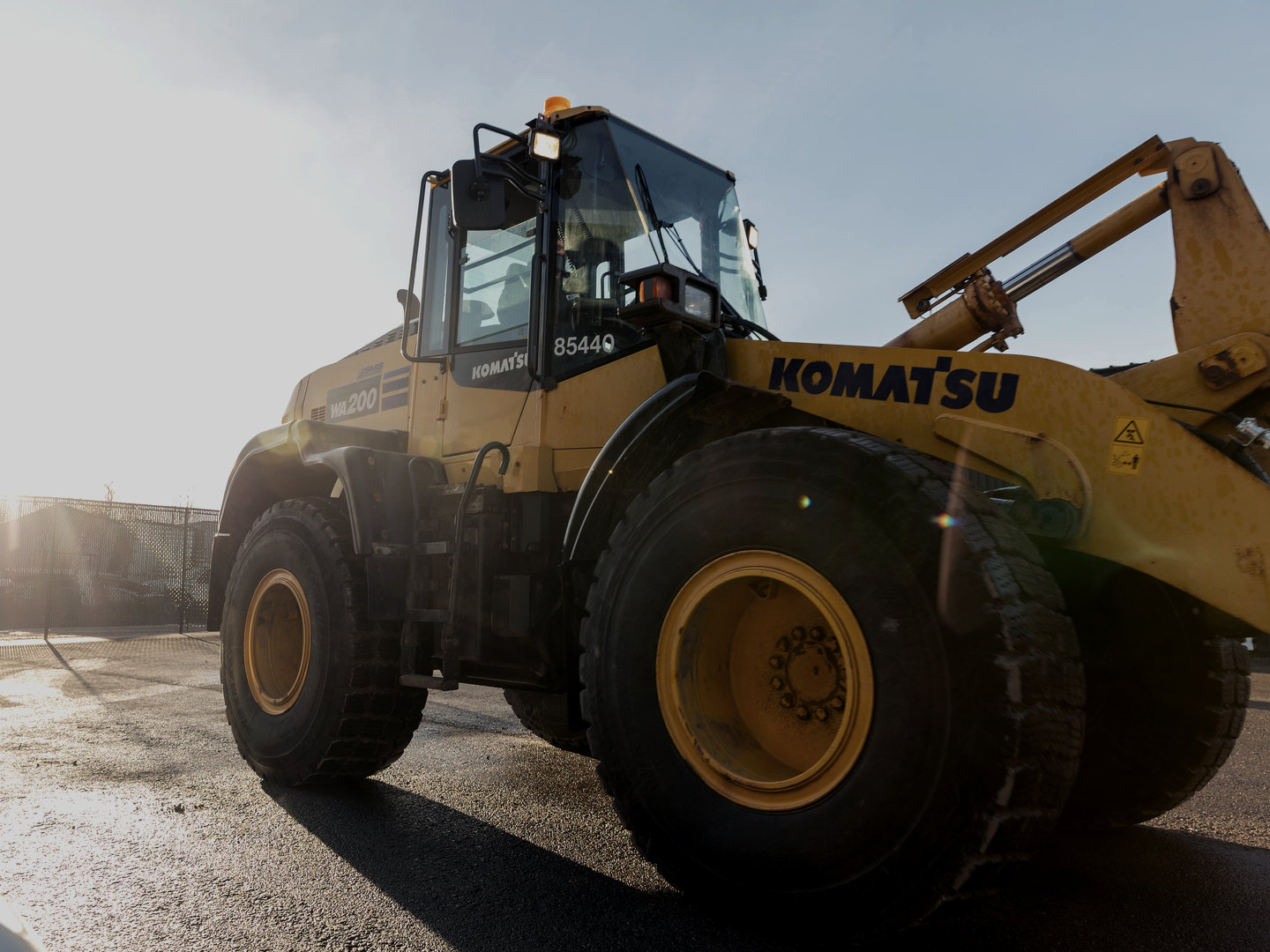A large wheel loader in the services company’s yard in Moncton, backlit by low sun on wet asphalt.