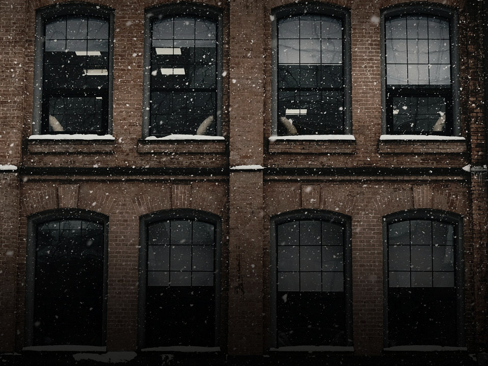 The brick front of an older building in falling snow, two rows of tall windows.