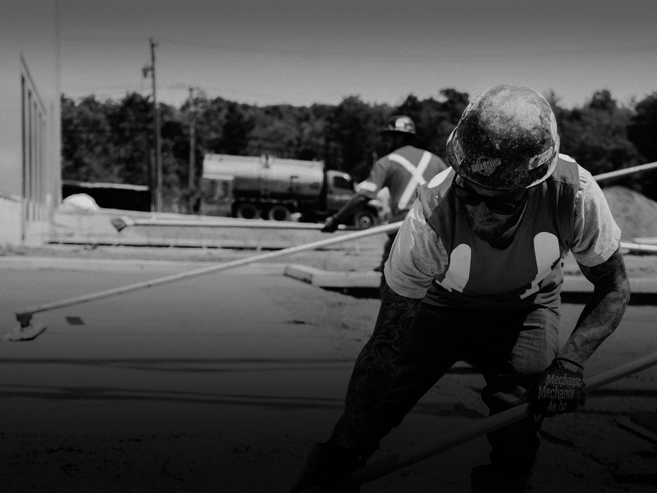 A crew member in a hard hat raking fresh concrete.