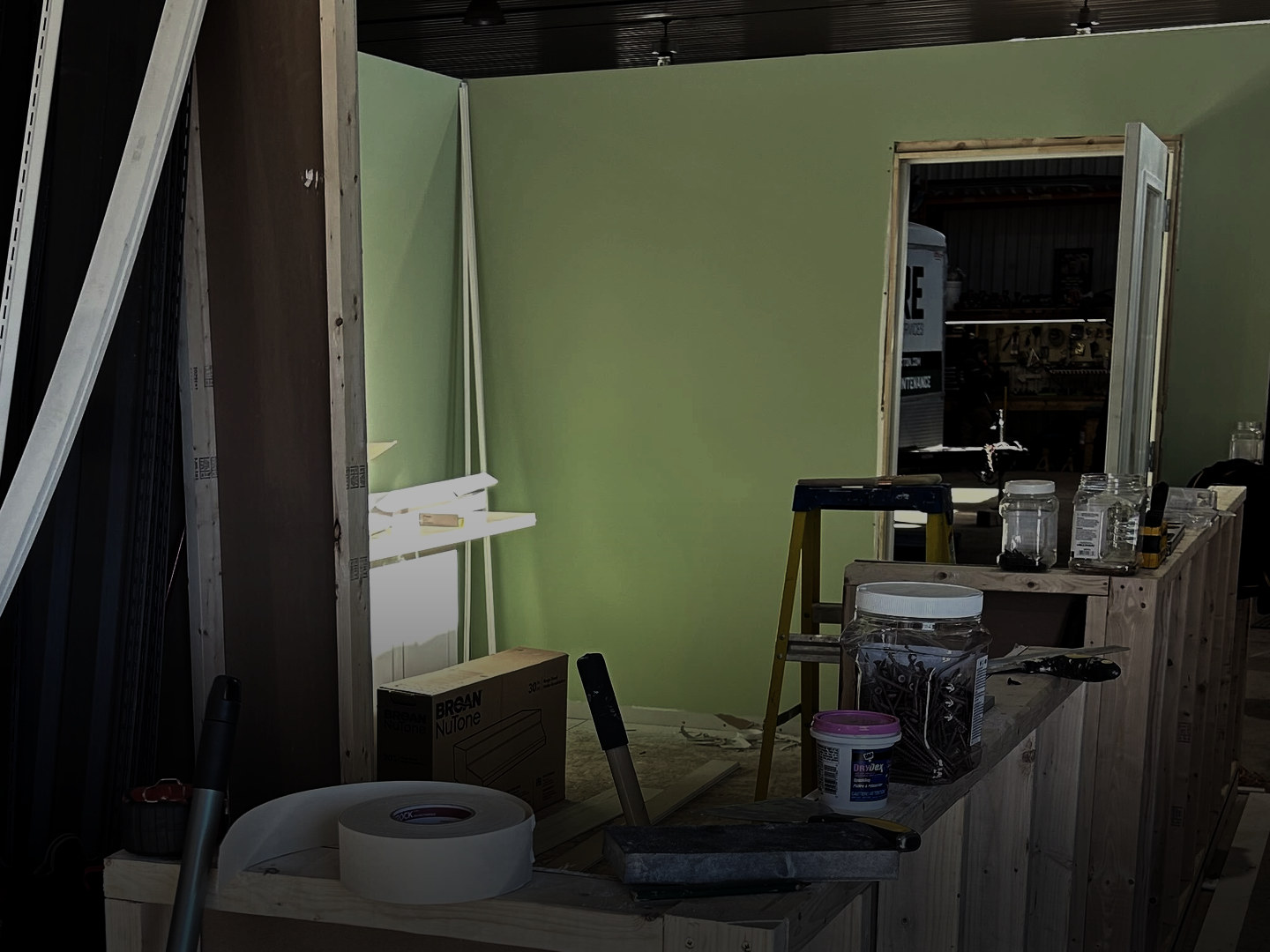 A wall freshly painted green behind a work counter with tape, filler and a stepladder.