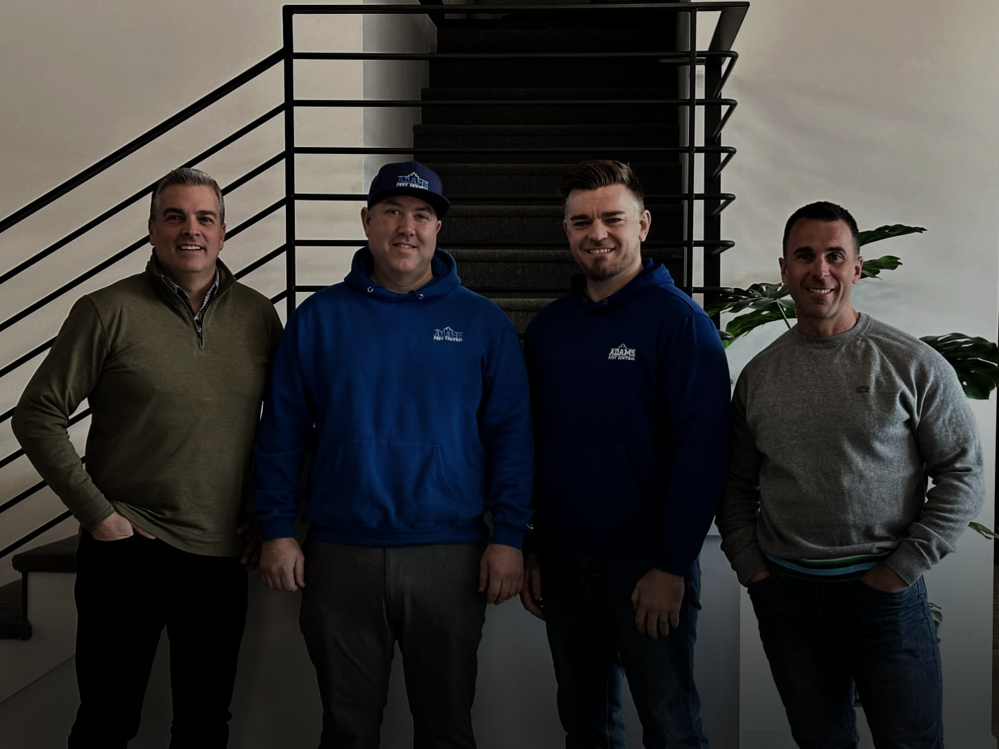 Tony LeBlanc with his three partners in the pest control company, standing in front of a staircase.
