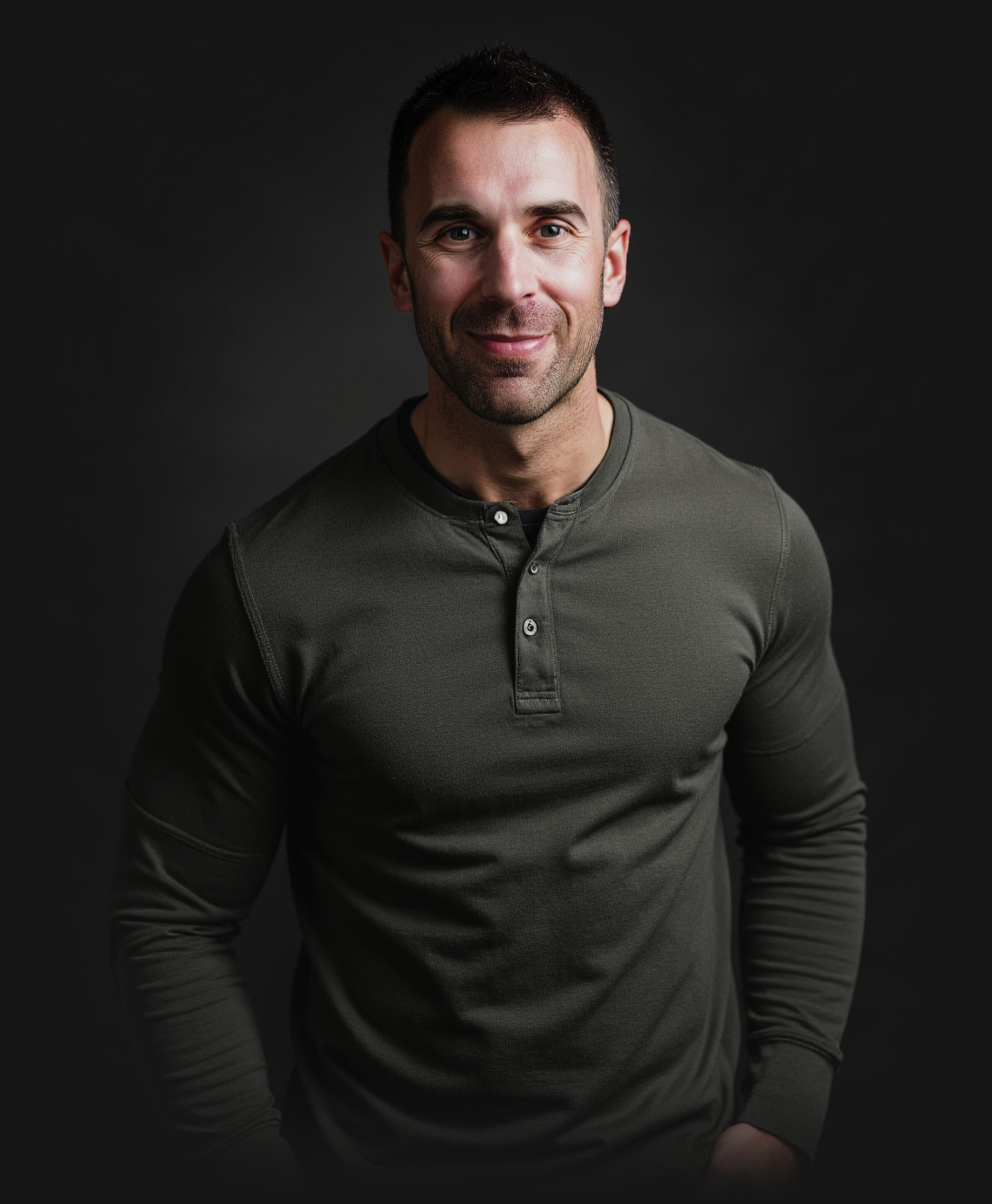 Tony LeBlanc in an olive henley against a dark studio backdrop, smiling, hands in his pockets.