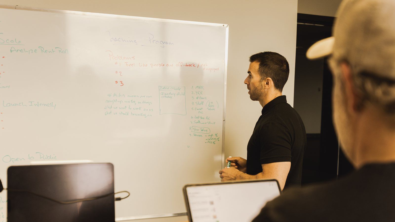 Tony at a whiteboard working through a plan, a team member in a cap in the foreground