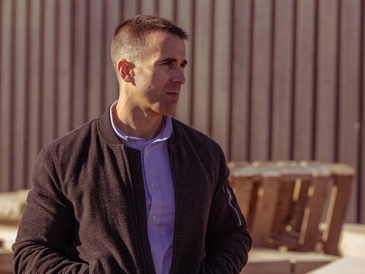 Tony LeBlanc in a brown jacket in a yard, looking to the right